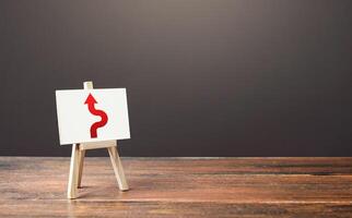 An easel with a red arrow avoiding an obstacle. Deviation from the route. Inevitability and inability to delay the inevitable. Purposefulness and perseverance, confident movement towards assigned goal photo