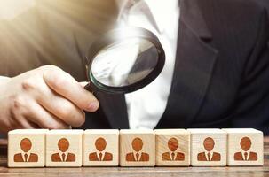 Businessman examines a magnifying glass blocks with employees. Analysis of company's work, optimization of personnel and costs. Checking for professional suitability of workers. Hiring and recruiting. photo