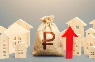 Russian ruble money bag and a city of house figures and red up arrow. Recovery and growth in property prices, high demand. Investments. Increase in revenues to municipal budget. Rent growth. photo