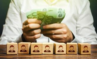 A man is counting euro money in his hands over blocks with symbols of employees. Wage fund. Accounting and budgeting. Payday. Expanding a profitable business, recruiting and training employees. photo