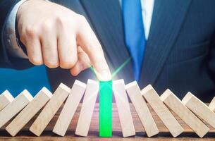 Businessman stops process of falling dominoes. Business systems processes recovery. Persistence strength and power. Risk management. Problem solving. Bankruptcy, debt restructuring refinancing. photo
