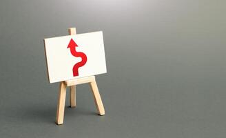 An easel with a red arrow avoiding an obstacle. Purposefulness and perseverance, confident movement towards the assigned goal. Maneuvering, taking right action. Deviation from the route, side mission. photo