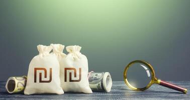 Israeli shekel money bags and magnifying glass. Budget revision. Monitoring of suspicious transactions, cash flows and the legality of the origin of capital. Finding financial resources, fund projects photo