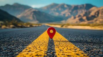 Red location pin marker stands out against yellow road line on empty desert highway, with mountain silhouettes and vibrant blue sky creating cinematic travel scene. orientation photo
