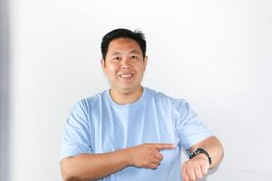 Happy face expression and smiling gesture of Asian man pointing his finger to his watch for being on time in important appointment or meeting. photo
