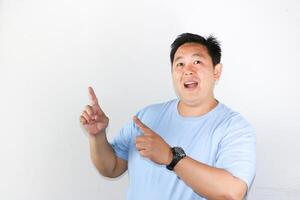 Happy Asian man showing happy face and wow expression pointing his finger to empty space. photo