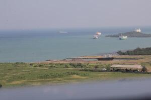 Several Cargo Ships Anchored off the Coastline Near Green Fields and Structures photo