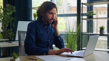 Arabian man hispanic businessman manager employer talk mobile phone search information on laptop check documents on desktop consulting client remote business consultation multitasking work in office photo