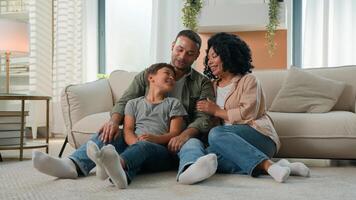 Multiracial happy family weekend African American mother and father with adopted Caucasian little boy child teen kid relax on floor home leisure together adult parents cuddling to son childcare love photo