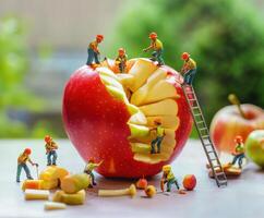 Miniature workers carefully sculpting and cutting an apple in a creative fruit art display photo