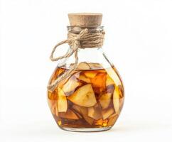 Unique glass bottle filled with amber-colored liquid and apple slices on white background photo