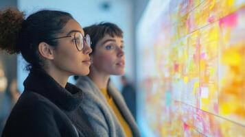 Side view of two participants engaged in a facetoface discussion while simultaneously sharing their ideas on a digital platform projected on a wall behind them photo