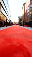 Elegant red carpet lined with barriers and spectators at a prestigious event in a modern urban setting during golden hour photo