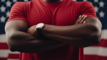 Strong man with crossed arms posing in front of an American flag while wearing a red t-shirt and watch photo