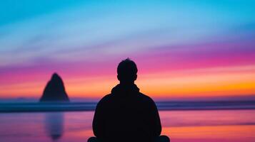 Meditation at sunset on a tranquil beach with colorful sky and distant rock formation photo