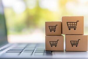 Online shopping process with small delivery boxes placed beside a laptop on a blurred outdoor background photo