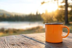 Bright orange mug resting on a wooden table near a lake at sunset with trees and mountains in the background photo