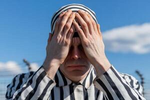 Man in striped prison uniform expresses despair under blue sky at historical site photo