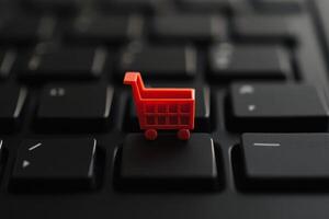 Small red shopping cart on black keyboard brings e-commerce into focus photo