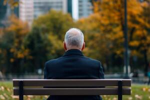 Elderly man sits quietly on park bench in autumn surrounded by colorful foliage in the city center during late afternoon photo