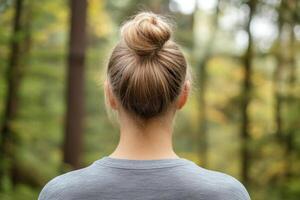 Woman with a bun hairstyle stands in a forest during autumn, surrounded by trees and golden leaves photo