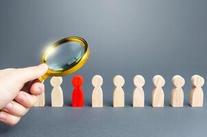 A hand with a magnifying glass studies a red person in a row of people. Identification, examination and isolation of potential carrier hostels of dangerous infections and diseases to prevent spread photo
