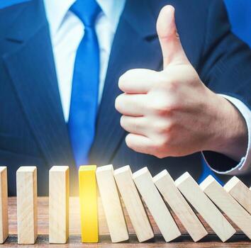 A businessman shows a thumbs up approval over a stopped process falling domino. Achieving success and completing a task. Solution. Cyber protection. Find a way stop the problem and prevent its spread. photo