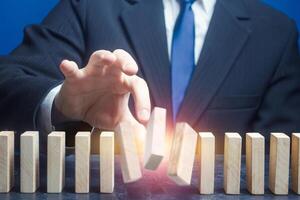 Man ruins order of standing domino row. Spoil plans, destroy business processes. Crime, destabilization of situation, break rules. Instability, hit a weak point. Sabotage, ruin a competitor's company. photo