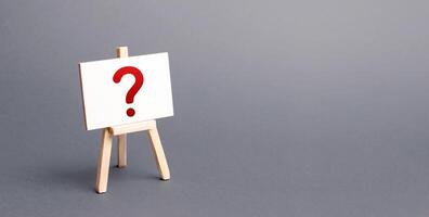 Easel with a question mark. Curiosity, mystery, investigation research. Poll Survey. Announcement of upcoming event, surprise. Unknown. Instability and uncertainty. No reaction or prognosis. photo