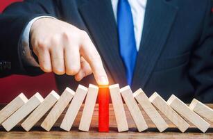 Businessman with a touch stops process of falling dominoes. Risk management concept. Successful strong business, problem solving. Stop destructive processes. Strategy development. Debt restructuring photo