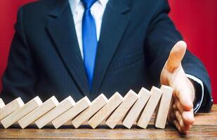 Businessman stops domino falling with his palm. Risk management concept. Successful strong business and problem solving. Stop the destructive processes. Strategy development. Debt restructuring photo