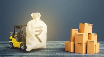Forklift truck carries indian rupee money bag near the pile of boxes. Superprofits. Investments financing in production, taxes, income revenues and costs. Profit from trade and exchange of goods. photo