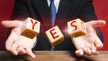 Cubes thrown by a man make up word YES. Agreement and acceptance, answer the question. Courage, irresistibility, zeal forwards, consent. Confirmation and approval. Important decision. Correct answer photo