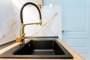 A beautifully designed kitchen features an elegant black sink paired with a sleek gold faucet, enhancing aesthetic and sophistication, transforming the space into a stylish culinary haven photo