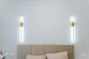 Two stylish light fixtures are elegantly mounted on the wall directly above the bed, which provides warm illumination and helps to create a cozy, inviting atmosphere in the entire room photo
