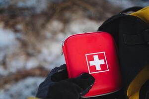 A person is firmly holding a brightly colored red first aid kit that features a distinctive white cross symbol, making it easily identifiable during emergencies for quick access photo