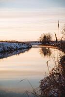 A serene river flowing gently, framed by lush trees along the shore, with a beautiful bridge gracefully arching in the background, all illuminated by the warm hues of sunset photo