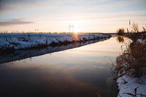 As the day comes to an end, the sun is slowly setting over the glistening snowy river, casting a warm glow on the icy landscape, creating a beautiful winter scene at dusk photo