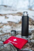 A first aid kit is currently resting on a rock next to a thermos, which is a type of vacuum flask commonly used to keep beverages hot or cold for extended periods of time photo