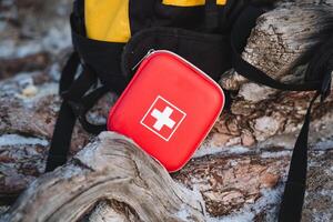 A bright red first aid kit is securely placed next to a sturdy backpack, ensuring that you are fully prepared for any emergencies that may arise during your outdoor adventures and travels photo