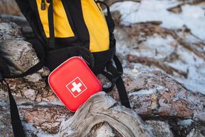 Next to a backpack, there is a prominently displayed red first aid kit featuring a white cross symbol on its exterior, which signifies its purpose for emergency medical assistance photo
