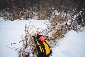 A bright yellow and black backpack is laying abandoned in the soft, cold snow, which creates a stark and striking contrast against the pristine white winter landscape surrounding it photo