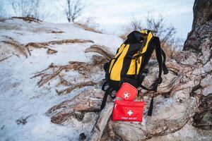 A bright yellow backpack is resting on a snowy hill, placed conveniently next to a vibrant red first aid kit, ready for any adventures that may lie ahead in the winter landscape photo