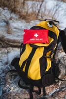 A bright and vibrant yellow backpack that is equipped with a red first aid kit on top is absolutely essential for all kinds of outdoor adventures, ensuring safety in case of emergencies photo