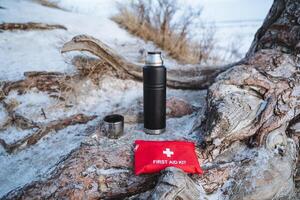 Resting on a substantial rock that is surrounded by untouched, pure snow, a first aid kit sits beside a thermos, both prepared for any emergencies or to enjoy a comforting hot beverage photo