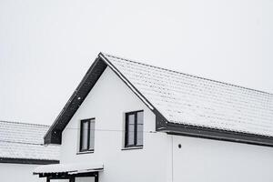 A charming white house adorned with a striking black roof is completely blanketed in soft, fluffy snow, creating a picturesque winter scene that captures the essence of the season photo