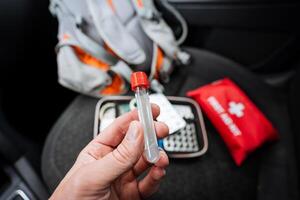 A person is skillfully holding a test tube in front of a first aid kit, showcasing the versatility of various items that can be found in medical and scientific environments photo