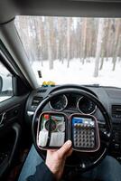 A person is comfortably sitting inside a parked car while holding a calculator in their hand, seemingly engaged in some calculations or planning on the device with focus and concentration photo