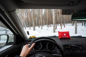 A person is actively driving a car, and there is a first aid kit conveniently placed on the dashboard for quick access in case of any emergencies that may arise during the trip photo