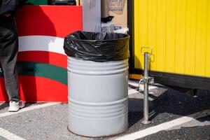 In a spacious parking lot, there is a trash can that has a black trash bag placed securely on top of it, making it easily visible for disposing of waste and maintaining cleanliness photo